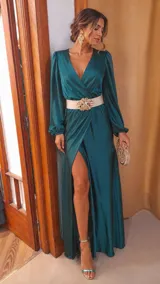 Vestido largo de satén color verde esmeralda, con escote cruzado en V, mangas largas abullonadas con puños elásticos y falda con tajo lateral profundo.
