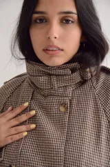 Chaqueta de corte estructurado con estampado cuadrille en tonos marrones y beige. Presenta cuello alto con tira ajustable, cierre frontal con botones, charreteras en los hombros y puños con detalle de hebilla.