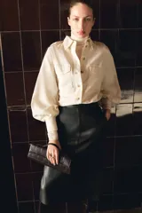 Camisa de estilo cargo color beige, confeccionada en mezcla de lino y algodón. Presenta cuello clásico, cierre frontal con botones, bolsillos superiores con solapa, charreteras en los hombros y mangas largas con puños abotonados.
