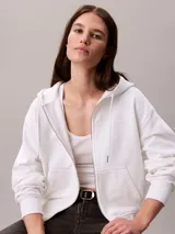 Buzo Calvin Klein de color blanco, con capucha ajustable mediante cordones, cierre frontal con cremallera y bolsillos tipo canguro. Presenta mangas largas y logo bordado en el pecho.