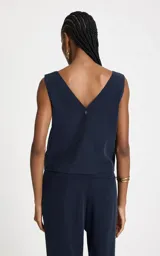 Blusa sin mangas color azul marino, con escote en V pronunciado, tirantes finos cruzados y detalle de argolla metálica central. Presenta un corte recto y caída ligera.