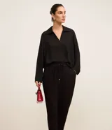 Pantalón de crepé rojo, modelo estilo pijama, de corte fluido, con cintura elástica y lazo de ajuste con terminales metálicas. Cuenta con bolsillos laterales y cierre frontal con cremallera y botón.