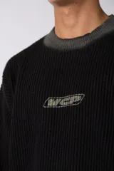 Sweater de punto acanalado con diseño degradado de negro a gris en el cuello y el ruedo. Presenta un corte regular y un pequeño bordado central en el pecho.