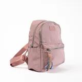 Mochila rosa de tela con cierre superior y bolsillo frontal con cierre. Tiene correas ajustables y un llavero decorativo.