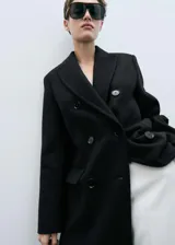 Abrigo largo de diseño oversize con doble botonadura, cuello con solapas de muesca y hombros caídos. Cuenta con dos bolsillos laterales y abertura posterior en el bajo.