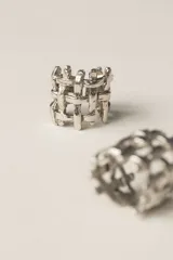 Anillo de diseño abierto con estructura de rejilla entrelazada, elaborado artesanalmente en metal con acabado plateado.