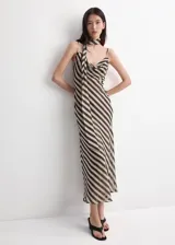 Vestido largo de fiesta con diseño de rayas diagonales en tonos beige y negro. Cuenta con tirantes finos, cuello drapeado y un adorno de fular incorporado en el cuello.