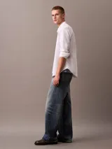 Camisa blanca de manga larga, confeccionada en tejido Oxford de algodón y elastano. Tiene cuello abotonado, cierre frontal con botones y logo de Calvin Klein bordado en el pecho. Corte regular.