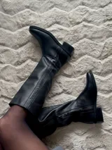 Bota de cuero vacuno color marrón, con caña alta, suela de goma y cierre lateral.