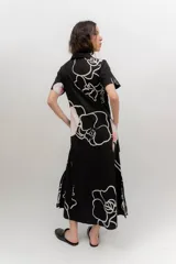 Vestido midi de popelina de algodón negra, con estampado floral en tonos rosados y blancos, cuello tipo bebe, mangas cortas, cierre frontal abotonado y bolsillos laterales.