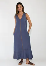 Vestido largo sin mangas de lino azul, con escote en V, bolsillos laterales y detalles de costuras marrones a la vista con terminaciones deshilachadas en el bajo.