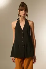 Chaleco largo negro, con escote halter y abertura frontal con botones joya. Corte entallado en la parte superior y ligeramente acampanado en el bajo.