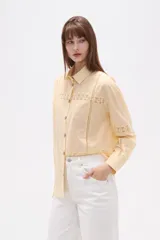 Camisa de algodón color blanco, de corte holgado y manga larga. Presenta detalles de encaje tipo puntilla en el frente, espalda y mangas, con cierre frontal de botones y cuello camisero clásico.