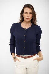 Saco de punto azul marino con cuello redondo, cierre frontal de botones y dos bolsillos delanteros tipo parche. Presenta mangas largas con puños acanalados y un diseño corto y estructurado.