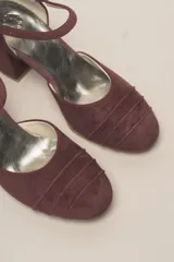 Zapato de tacón color bordó, confeccionado en terciopelo suave, con diseño de pulsera en el tobillo y cierre de hebilla. La punta es cerrada y presenta detalles de líneas cosidas. El tacón es ancho y forrado, con una altura de 7 cm.