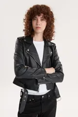 Campera biker negra de cuero sintético con cuello solapa, cierre cruzado con cremallera, bolsillos con cremallera y cinturón ajustable.