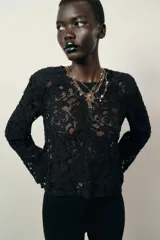 Top de encaje negro con cuello redondo, manga larga y hombreras incorporadas. Presenta un diseño de corte recto y cierre posterior.
