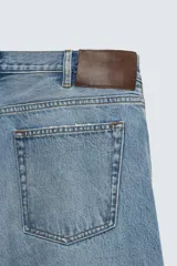 Jeans de mezclilla rígida de algodón, color azul claro con efecto lavado y ligero desgaste. De tiro medio, corte recto desde la cadera hasta la rodilla y ligeramente acampanado en el bajo (bootcut). Cierre frontal con botonadura y cinco bolsillos.