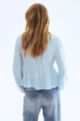 Blusa celeste con estampado de lunares blancos, escote en V pronunciado con volados, mangas largas abullonadas con puños elásticos y lazo ajustable en el frente.