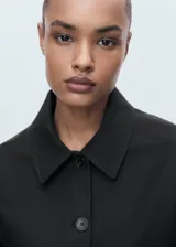 Chaqueta corta de corte recto con cuello camisero, cierre frontal de botones y dos bolsillos de parche laterales. Presenta mangas largas y forro interior.