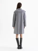 Tapado de tejido de punto color gris, con cuello tipo solapa grande, cierre frontal con botones a presión y bolsillos frontales. Presenta costuras decorativas visibles y diseño de largo medio.