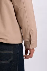 Campera color taupe de corte recto, con cuello camisero de pana marrón oscuro, cierre frontal oculto con botones a presión y grandes bolsillos frontales con solapa.
