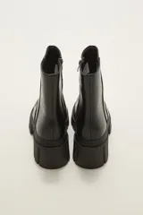 Bota de caña media en cuero sintético color negro, con suela track dentada y cierre lateral interno.