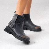 Bota corta estilo chelsea de cuero vacuno negro con acabado desgastado en tono marrón en la puntera y laterales. Presenta elástico lateral, cierre interno y suela de goma tipo track con plataforma.