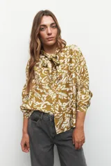 Camisa color verde oliva con estampado orgánico en blanco, de manga larga con puños abotonados, cuello con lazo y cierre frontal con botones.