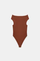 Body de tejido liso color terracota, con escote recto que deja los hombros descubiertos y mangas cortas. Cierre inferior con botones a presión.