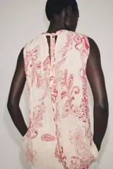 Top sin mangas confeccionado en hilatura de viscosa, con cuello redondo y cierre en la espalda con abertura y botón. Presenta un diseño con estampado paisley a contraste en color rojo sobre fondo beige.