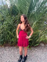 Vestido corto color bordó con escote en V, diseño de top triangular y aberturas laterales en la cintura. Presenta breteles finos cruzados en la espalda y falda con doble volado irregular en el ruedo.
