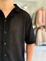 Camisa de manga corta negra con tejido texturizado tipo red, cuello camisero y cierre frontal con botones.