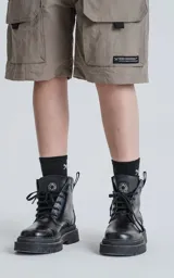 Bermuda técnica color arcilla (marrón claro/beige) de calce oversize, confeccionada en poliéster liviano. Presenta múltiples bolsillos cargo con tapa y un cinturón de ajuste con hebilla plástica negra. Incluye detalles reflectivos.