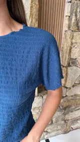 Blusa de manga corta color azul oscuro con textura arrugada o plisada, cuello redondo con borde festoneado.