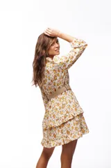 Vestido corto con estampado floral amarillo y blanco, mangas largas abullonadas y falda con volados. Incluye cinturón de soga.