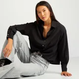 Camisa negra de corte holgado con cuello clásico y mangas largas con puños abotonados.