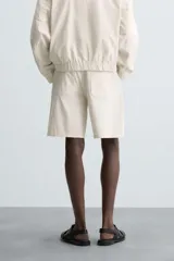 Bermuda de algodón color beige claro con rayas verticales finas en tono más oscuro. Diseño de corte regular con bolsillos delanteros y bolsillos traseros de plastrón.