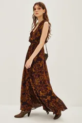 Vestido largo sin mangas con escote en V profundo y lazo ajustable en la cintura. Presenta un estampado geométrico en tonos marrón y ocre sobre fondo oscuro, con falda amplia y fluida.