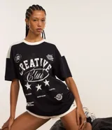 Remera oversized negra con mangas y cuello blanco, con estampado frontal que incluye la frase "Creative Club" en blanco, estrellas y otros gráficos en estilo vintage.