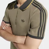 Chomba Adidas de manga corta en color verde militar, con cuello polo negro de bordes amarillos y cierre frontal parcial. Cuenta con las clásicas tres tiras en los hombros y mangas, y el logo del trifolio bordado en el pecho.