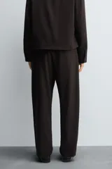 Pantalón regular fit color marrón oscuro, confeccionado en tejido con viscosa. Cuenta con cintura elástica, bolsillos delanteros y detalle de bolsillos traseros de vivo. El cierre frontal es con cremallera y botón.