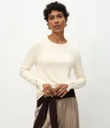 Suéter Cortelle de punto color beige, con cuello redondo, manga larga y detalle de botones metalizados en los puños.