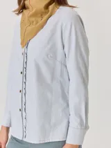 Bandana de forma triangular en tono gris oscuro con estampado de cuadros sutiles. Presenta detalles de pespuntes a mano en hilo naranja y blanco, junto con pequeños apliques decorativos que le otorgan un estilo artesanal y único.