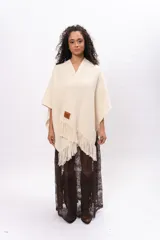 Ruana de tejido de punto en color crudo, con diseño abierto, flecos en el borde inferior y etiqueta de cuero con la marca Pura Lana en el frente.