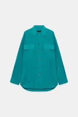Camisa de corte fluido con cuello solapa y manga larga. Presenta cierre frontal con botones y dos bolsillos de plastrón con solapa en el pecho. El diseño cuenta con bajo redondeado y costuras verticales decorativas.