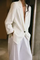 Blazer blanco de lino con cuello solapa, manga larga con hombreras y puños con vuelta estampada. Tiene bolsillos delanteros con solapa y cierre frontal con botón.