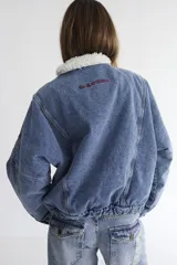 Campera bomber de denim azul oscuro con costuras a contratono en color verde. Presenta cuello de corderito en color marrón, cierre frontal y diseño holgado.