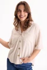 Camisa de lino color beige, de manga corta, con cuello camisero, bolsillos delanteros con solapa y cierre frontal con botones de madera.