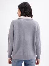 Campera de tejido de punto en color gris, con cierre frontal completo y cuello alto. Presenta un diseño de canalé vertical y puños con detalle en contraste.